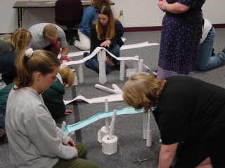 Photo of several college students on the floor of a classroom building bridges made of paper.